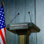 Press podium with microphones and American flag in the background