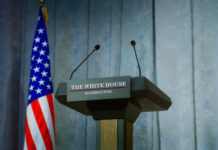 Press podium with microphones and American flag in the background