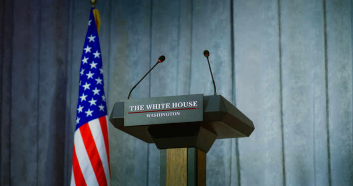 Press podium with microphones and American flag in the background