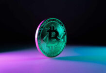 A shiny Bitcoin coin illuminated with colorful lighting against a dark background