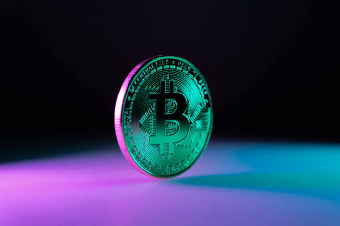 A shiny Bitcoin coin illuminated with colorful lighting against a dark background