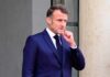 Emmanuel Macron in a suit, standing outdoors with a thoughtful expression