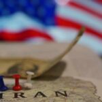 Map of Iran with push pins and a dollar bill in front of an American flag