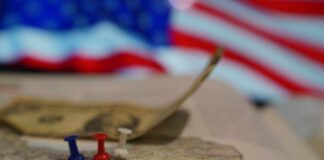 Map of Iran with push pins and a dollar bill in front of an American flag