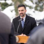 Man in formal attire speaking at a podium during a winter event