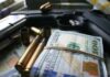 A handgun surrounded by cash and bullet casings