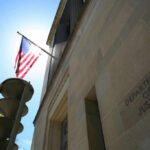 The Department of Justice building with an American flag and sunlight in the background