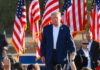 A speaker at a political rally surrounded by American flags and an engaged crowd