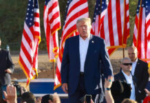 Senators FUME Over Trump’s Bold Memorial Day Clash A speaker at a political rally surrounded by American flags and an engaged crowd