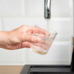 A hand holding a glass under a kitchen faucet as water is being poured into it