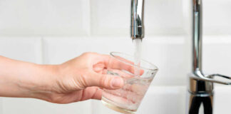 A hand holding a glass under a kitchen faucet as water is being poured into it