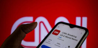 A hand holding a smartphone displaying the CNN news app against a red background
