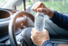A person opening a water bottle while holding the steering wheel of a car