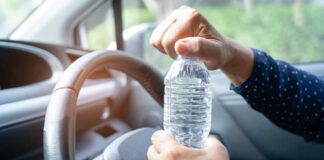 A person opening a water bottle while holding the steering wheel of a car