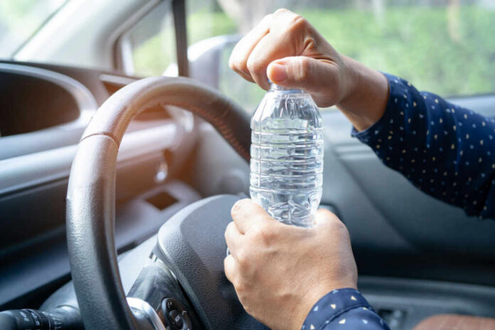 A person opening a water bottle while holding the steering wheel of a car
