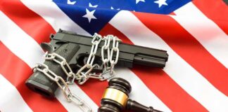 A handgun chained and placed on an American flag with a gavel nearby