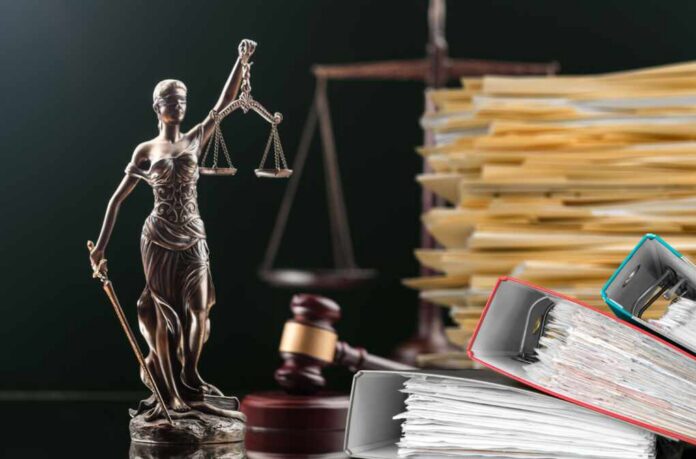 A bronze statue of Lady Justice holding scales, with legal documents and a gavel in the background
