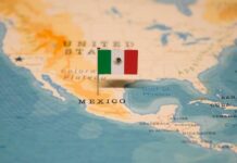 Mass Displacement: Cartel Warfare in Mexico Map of North America with a flag of Mexico pinned on it