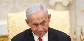 A government official with a serious expression seated in a formal setting