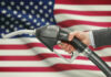 A hand holding a fuel pump in front of an American flag