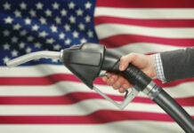 A hand holding a fuel pump in front of an American flag
