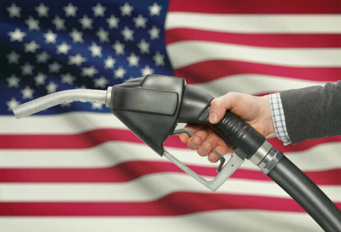 A hand holding a fuel pump in front of an American flag