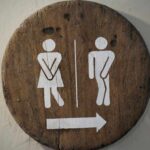 Wooden restroom sign indicating mens and womens facilities with directional arrow