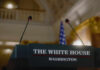 Press podium with microphones and an American flag in the background