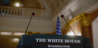 Press podium with microphones and an American flag in the background