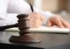 A gavel on a desk with a blurred hand writing in the background