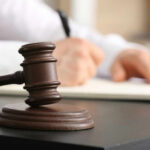 A gavel on a desk with a blurred hand writing in the background