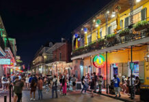 Crowded street on Bourbon Street at night with colorful lights and people socializing