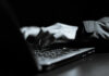 Close-up of hands typing on a laptop keyboard in a dark setting