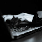 Close-up of hands typing on a laptop keyboard in a dark setting