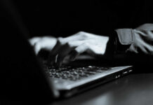 Close-up of hands typing on a laptop keyboard in a dark setting
