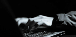 Close-up of hands typing on a laptop keyboard in a dark setting