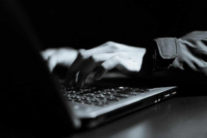 Close-up of hands typing on a laptop keyboard in a dark setting