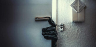 A gloved hand reaching through a partially opened door