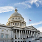 The U.S. Capitol building with a dome and American flag against a blue sky