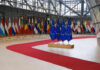 EU Crackdown Erupts: ‘Send Them Back’ Chants Flags of European countries displayed in a modern hall with a red carpet
