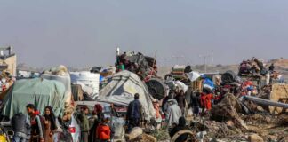 Displaced families with belongings crowd a rubble-strewn road