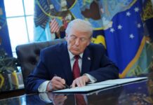 A person in a suit signing documents at a desk in the Oval Office