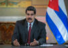 Man speaking at podium with Cuban flag in background.