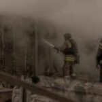 Missiles Obliterate Kyiv Grocery Hub Firefighters spray water into a smoke-filled structure