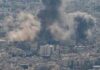 Smoke plumes rise over a dense cityscape