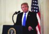 man at podium with microphone and US flag