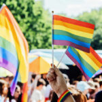 Church Pride Sponsor Ignites Doctrinal Meltdown A hand holding rainbow flags at a pride event with a crowd in the background