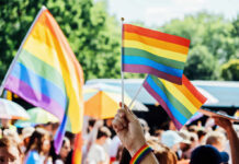 Church Pride Sponsor Ignites Doctrinal Meltdown A hand holding rainbow flags at a pride event with a crowd in the background