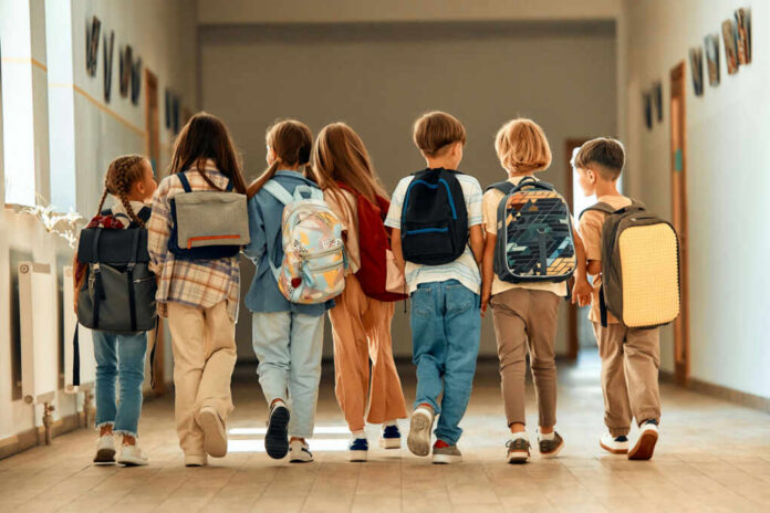 shutterstock_2359643391 A group of children walking together in a school hallway, each carrying a backpack