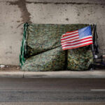 A makeshift shelter draped with an American flag next to a shopping cart on a city street
